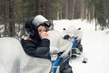 Woman having a hot drink on a snowmobile