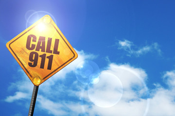 Yellow road sign with a blue sky and white clouds: call 911