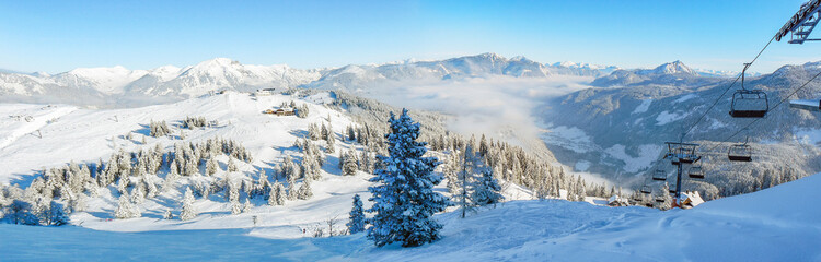 Fototapeta Alpine ski slope mountain winter panorama with ski lift,skiers and snow covered forest. obraz