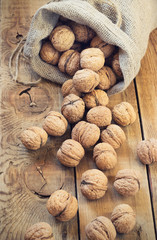 Pile of walnuts in shell inbag on a wooden background