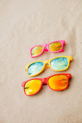 Fototapeta na wymiar sunglasses for Family. Red, pink, yellow sunglasses on the sand background. Family sunglasses on the beach with reflection of sky and trees