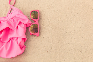 Pink swimwear on the sand with pink sunglasses. Pink swimwear on the beach and pink sunglasses with reflection of sky. Pink swimwear on the sand with pink sunglasses closeup