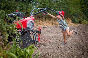 Harvesting on the farm. Child controls the red tractor on the garden. Baby girl driver the tractor