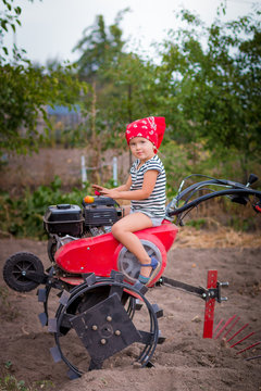 Child drives the tractor. Baby girl with red bandana on the red tractor in the garden. Harvesting on the farm