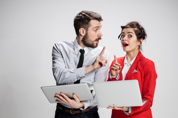 The young businessman and businesswoman with laptops  communicating on gray background