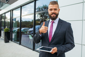 Fototapeta na wymiar Young bearded businessman using tablet pc outside the office. Th