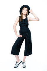 cute brunette woman in black overall and hat in studio on white background