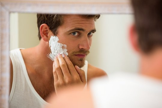 Young man applying shaving foam on his face