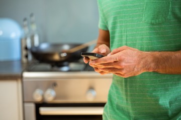 Mid section of man using mobile phone in kitchen