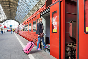 Woman tourist with suitcase sits on train at railway station