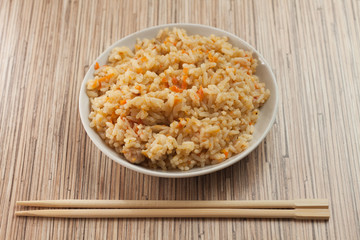 bowl of cooked rice with chopsticks on the bamboo textured table