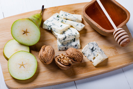 Blue cheese with slices of pear, nuts and honey on bamboo wooden cutting board.