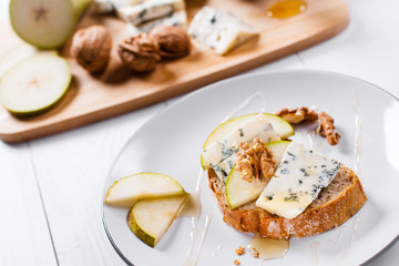 Sandwich with Blue cheese with slices of pear, nuts and honey on bamboo wooden cutting board.