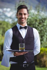 Handsome waiter holding a tray with glass of whiskey