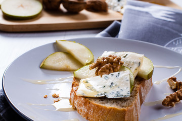 Sandwich with Blue cheese with slices of pear, nuts and honey on plate.