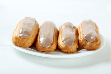 Eclairs with glaze on a white wooden table