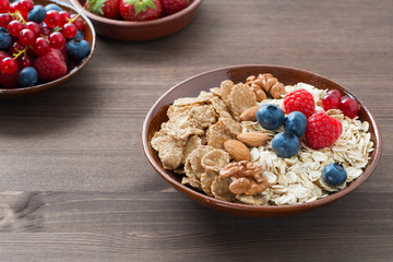 oatmeal and muesli in a bowl, fresh berries on wooden background