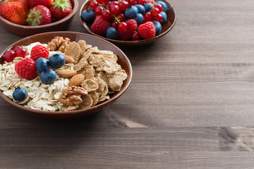 oatmeal, granola, nuts and berries in bowls on wooden background