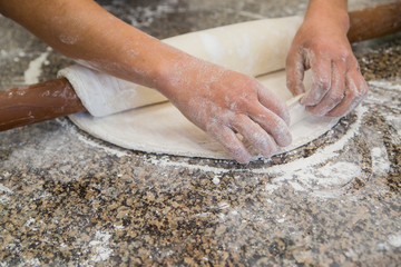 Hands baking dough with rolling pin on wooden table