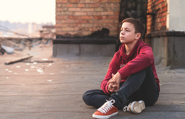 serious teenager sitting on the roof of the house
