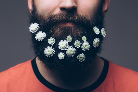 Close-up of young shirtless man with flowers in his beard standing against grey background