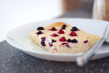 Appetizing cottage cheese casserole with wild berries in a white plate on a gray table, closeup, selective focus