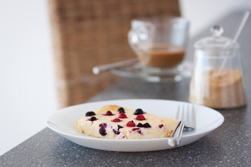 Appetizing cottage cheese casserole with wild berries in a white plate on a gray table, closeup