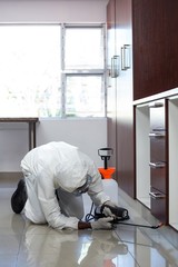Pest control man spraying pesticide under the cabinet