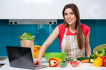Young beautiful woman using a tablet computer to cook in her kitchen