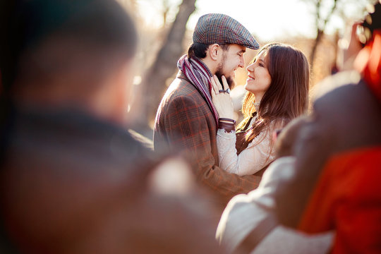 Stylish Old Fashioned Couple Among Crowd Looking At Each Other Outdoors In Backlight. Man Wearing Tweed Flat Cap, Brown Clothes.