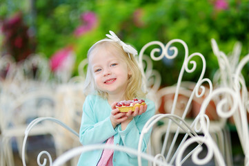 Adorable little girl eating fresh sweet strawberry cake outdoors on warm and sunny summer day