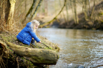 Adorable girl playing with a stick by a river