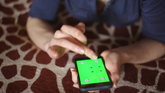 Young woman playing with Apple iPhone 6S at home on giraffe bedcover green screen ready (hands only)