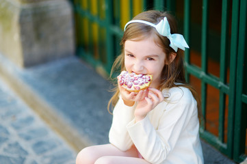 Adorable little girl eating fresh sweet strawberry cake outdoors on warm and sunny summer day
