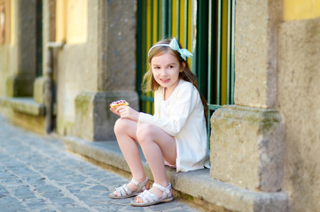 Adorable little girl eating fresh sweet strawberry cake outdoors on warm and sunny summer day