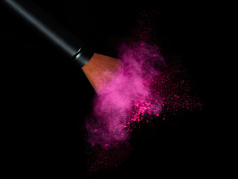 Cosmetics brush with glowing face powder. Dust explosion
