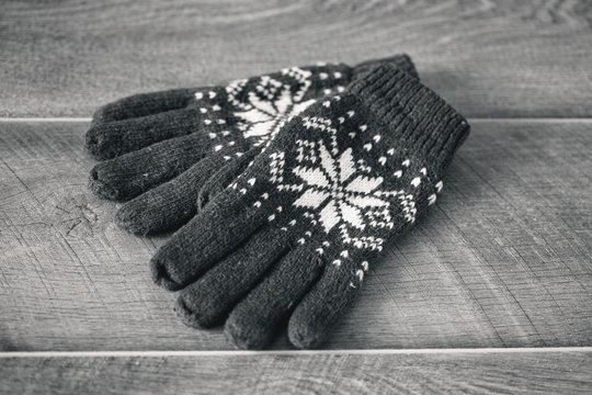 knitted gloves with embroidered snowflakes on wooden background, rustic style, top view