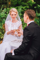 Groom and bride drinking champagne on a table in a decorative autumn forest, happy newlyweds