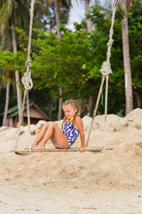girl with two braids in a bathing suit on a swing on the beach