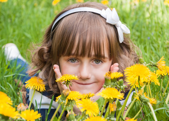 Little cute smiling girl on the lawn among dandelions