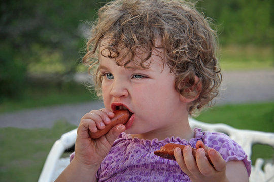 Young girl eating greasy hot dog with her hands. Messy tangled hair.