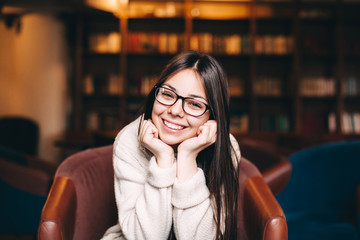 Smiling student sitting against bookshelves.