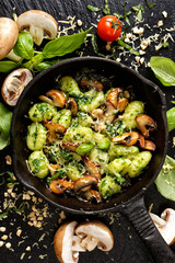 Italian dish, potato gnocchi with addition of herb pesto, cheese and mushrooms on cast iron frying pan