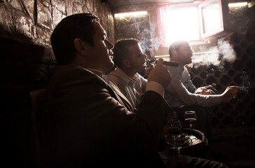 Obraz na płótnie Canvas Three businessmen sitting in the wine cellar drinking wine and smoke cigar, resting after a hard day at work.