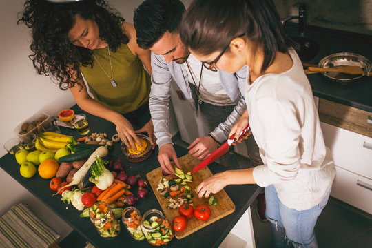 Young Group Of Friends  In Kitchen Preparing Together Vegetarian Meal.Preparing Fruit Salad.