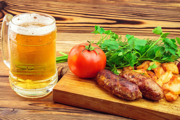 Grilled meat sausages with fried potatoes, fresh produce and mug of beer on wooden board