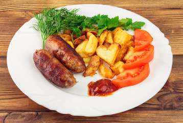 Grilled meat sausages with fried potatoes, sliced tomatoes, fresh produce and ketchup in plate on wooden table