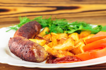 Grilled meat sausages with fried potatoes, sliced tomatoes, fresh produce and ketchup in plate on wooden table