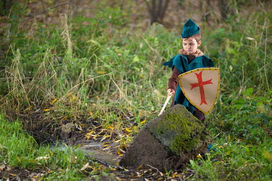 Cute little boy dressed as a knight trying to remove the magical Excalibur sword from the stone