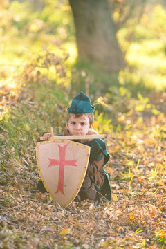 Cute little knight playing with a sword and a shield hiding in the forest